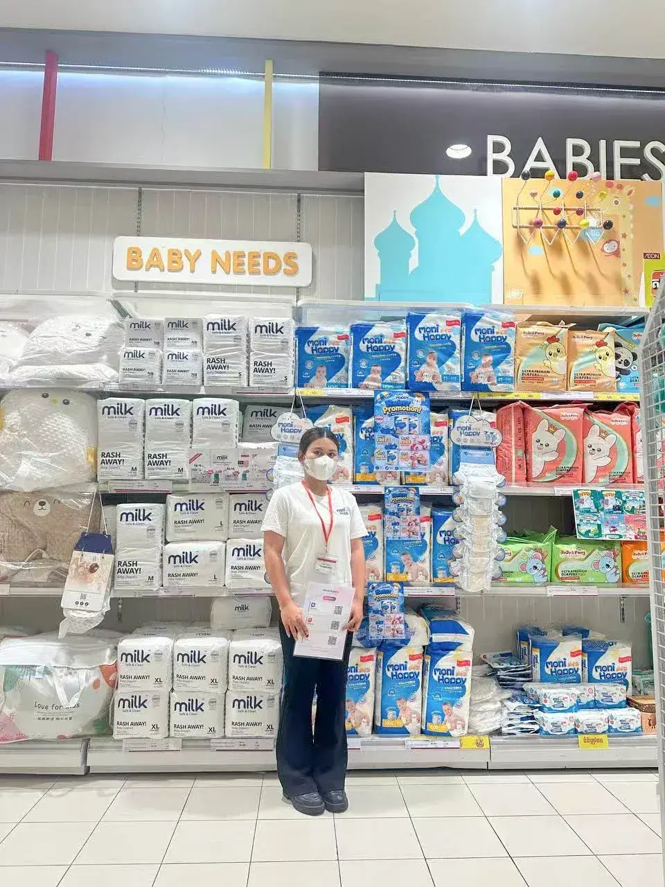 Moni Happy products displayed in BABY NEEDS section of Cambodia supermarket, brand promoter standing beside full product range on shelves
