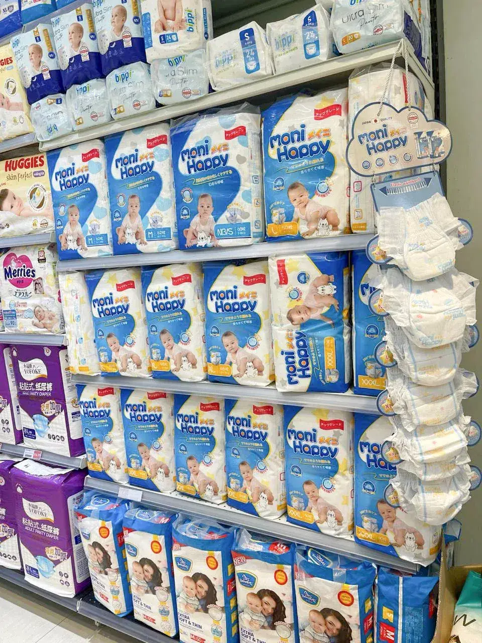 Moni Happy diapers on retail shelf alongside competing brands in Cambodia supermarket, JAPAN QUALITY cloud signage and product samples visible