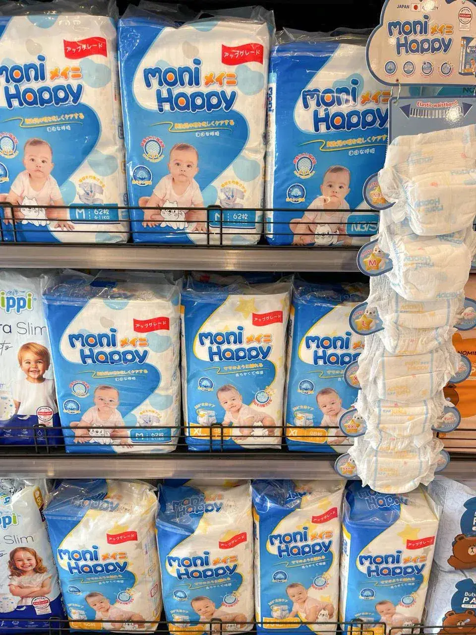 Moni Happy tape diapers and pants diapers on shelf in Cambodia baby store, full size range NB through XL with JAPAN QUALITY labeling