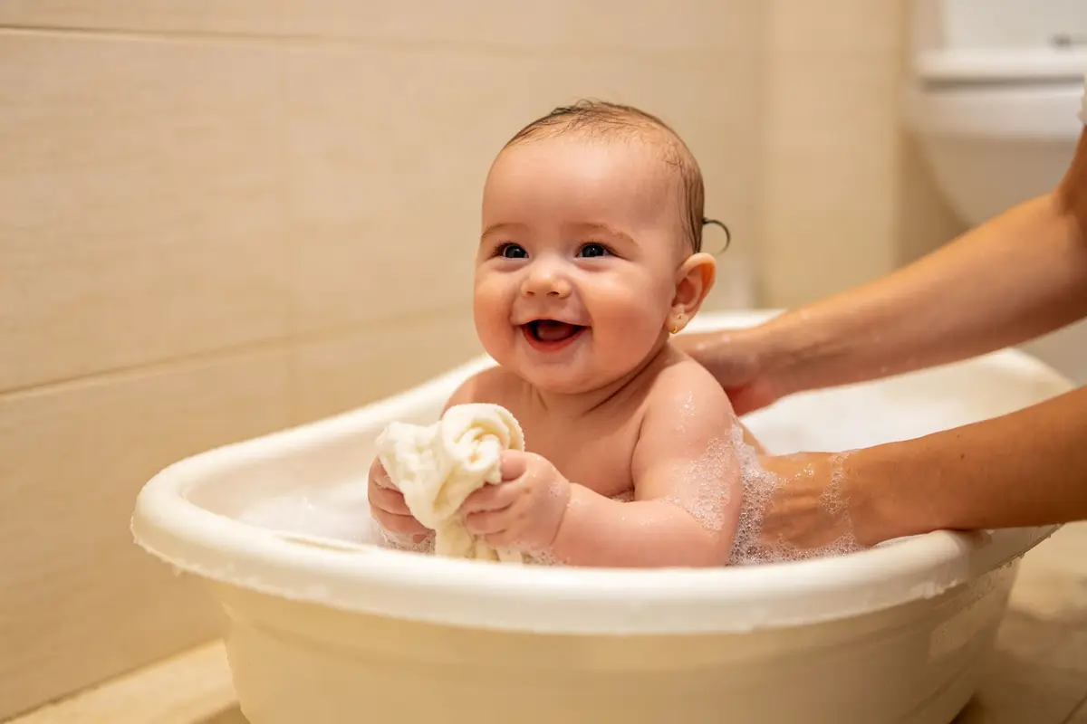 Happy baby bathing in small tub with mother washing gently
