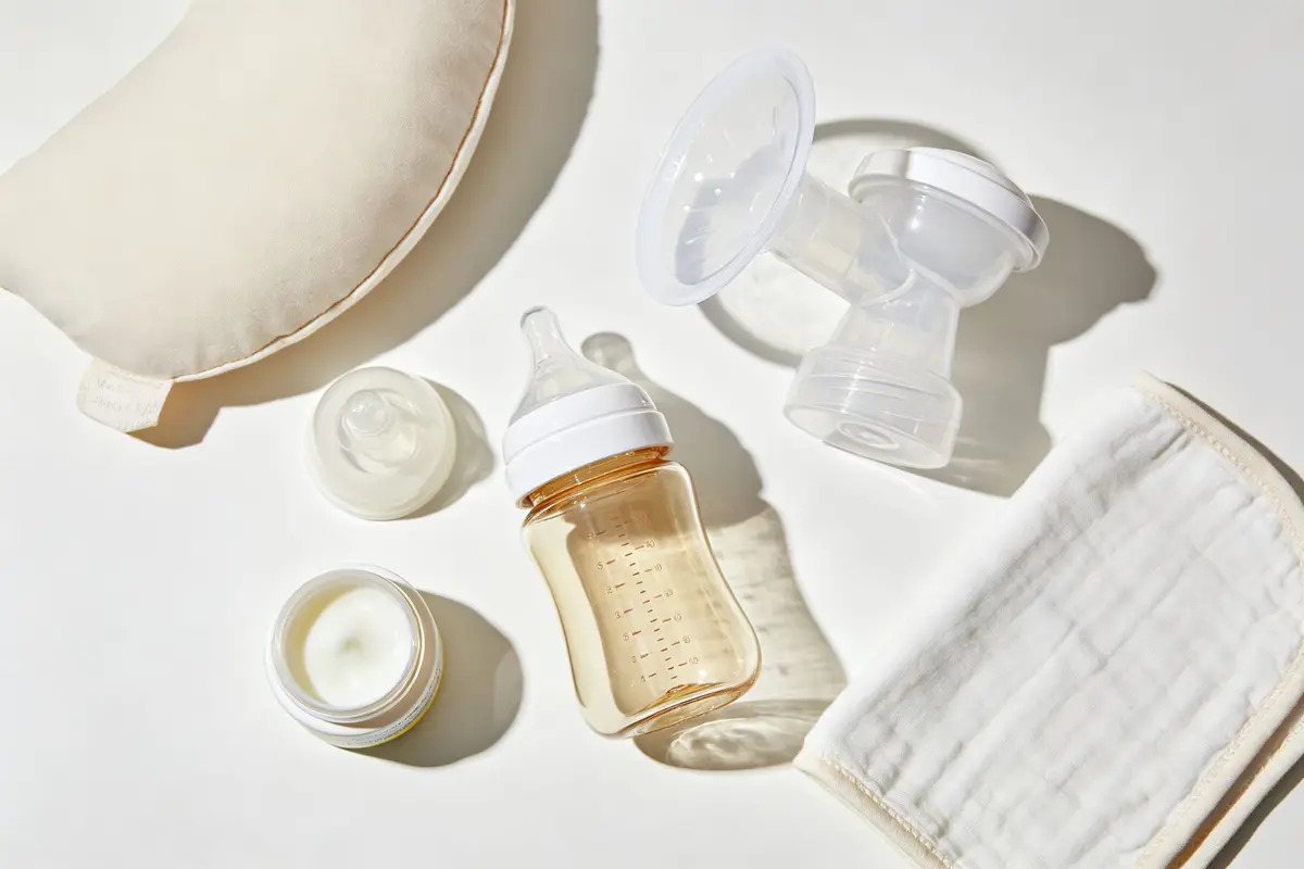 Baby feeding essentials including bottle breast pump parts burp cloth and nursing pillow on white surface
