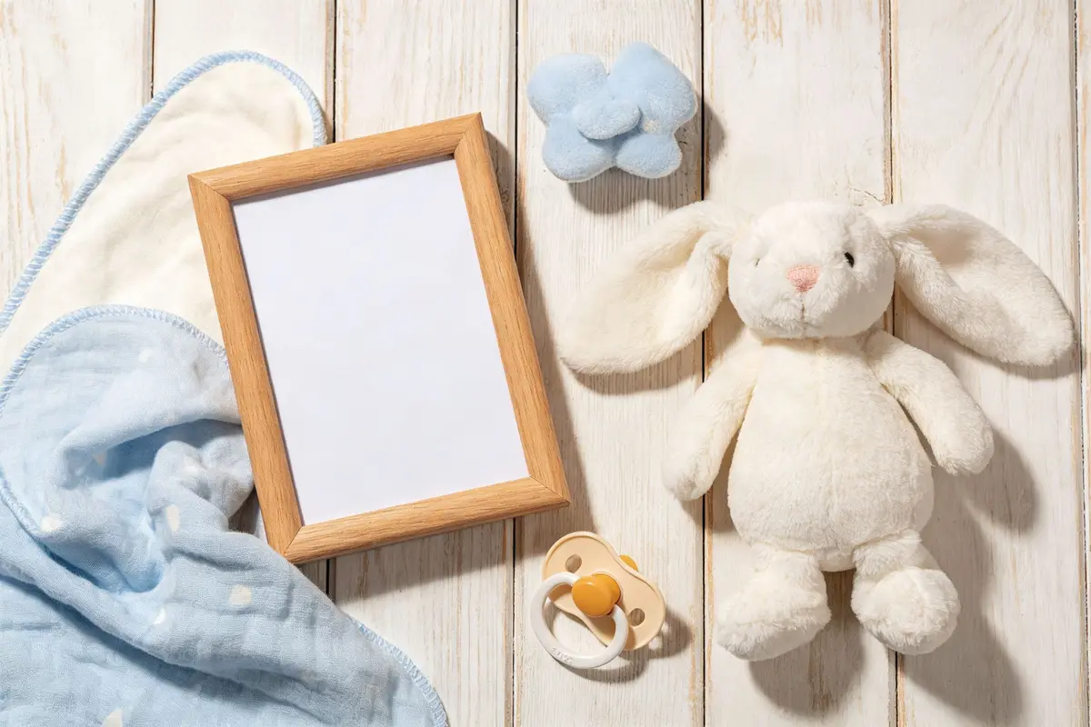 Baby comfort items including security blanket, plush rabbit, wooden photo frame, and pacifier on light wooden surface