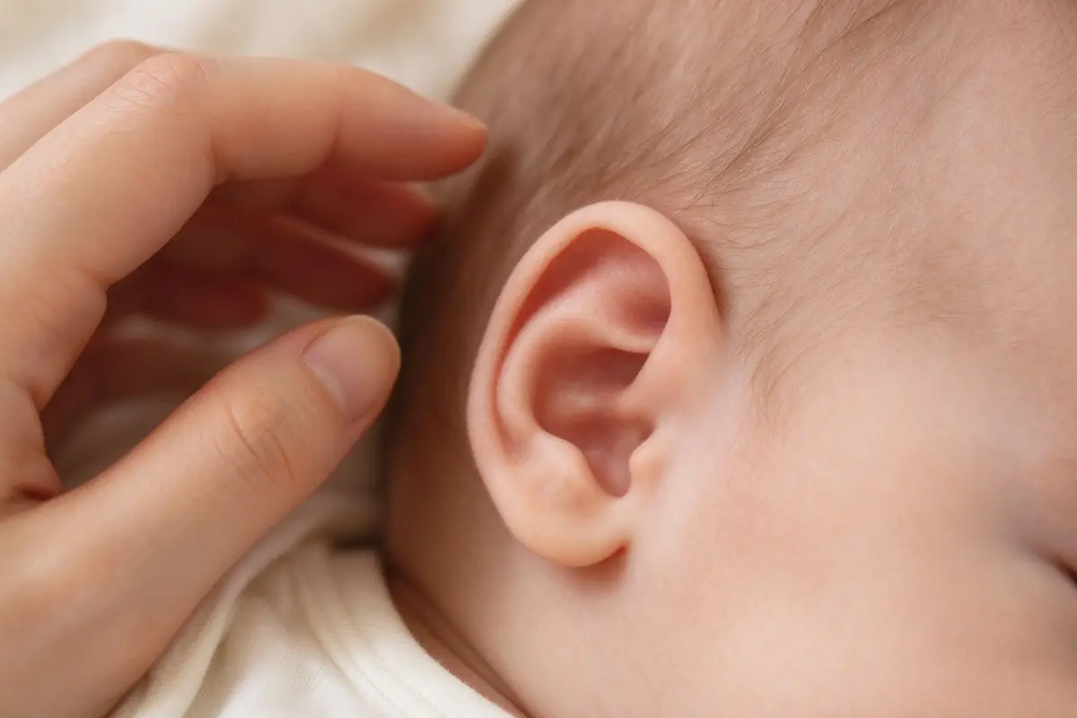 Close-up of newborn baby ear with parent's hand gently nearby, soft warm light