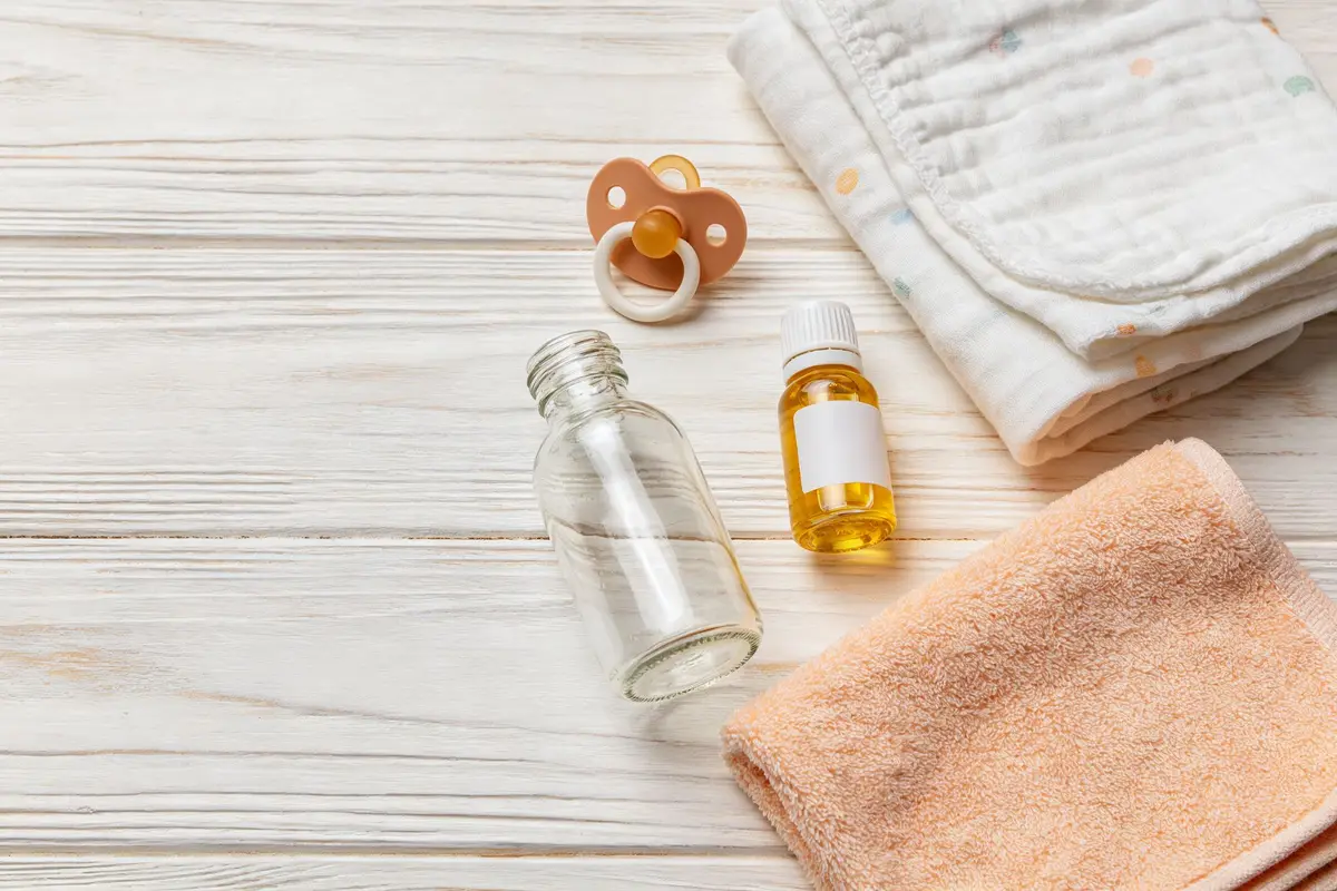 Baby colic soothing items including glass bottle, pacifier, muslin swaddle, massage oil, and washcloth on wooden surface