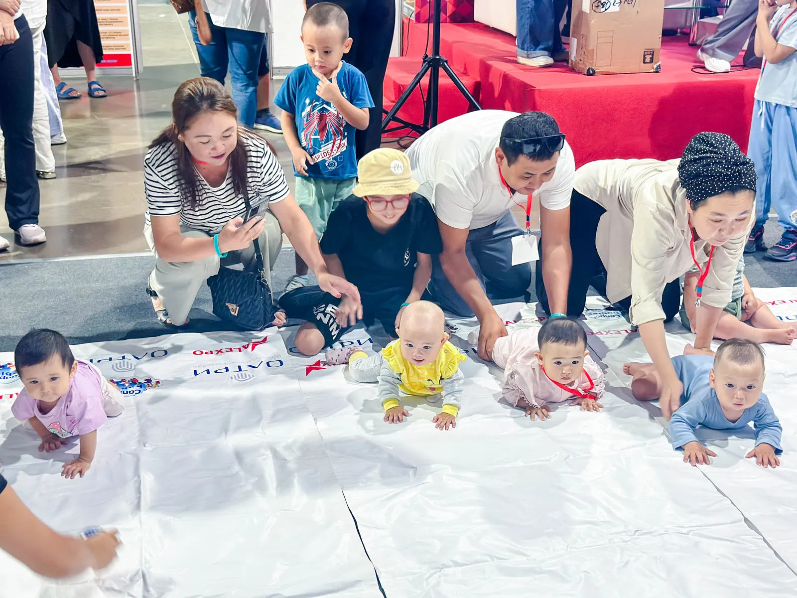 The Baby Crawling Race at the Kazakhstan Expo — babies racing on the white track while parents cheer and film from the sidelines.