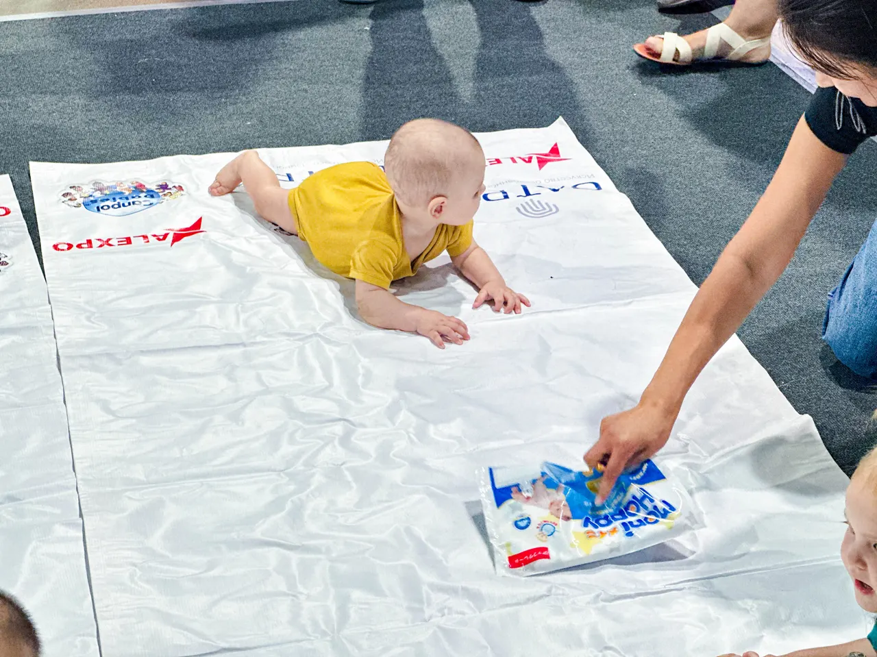 A determined little racer crawling towards a Moni Happy gift package during the Baby Crawling Race at the Kazakhstan Expo.