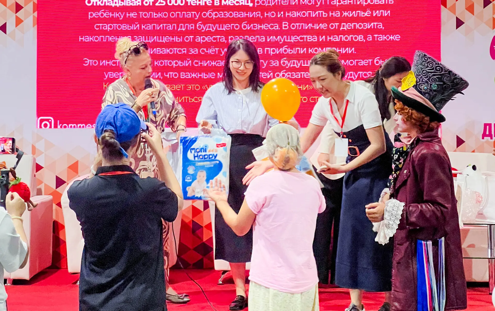 A packed stage moment at the Kazakhstan Baby & Kids Expo — Moni Happy gift packages presented to winning families amid balloons and cheers.