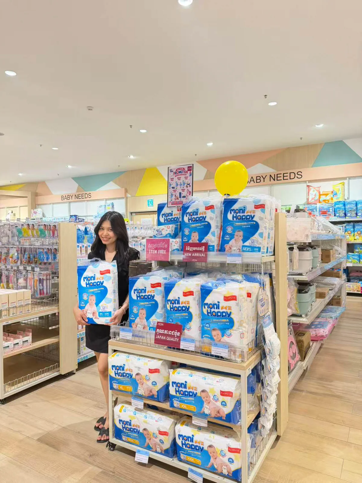 Staff member beside a Moni Happy diaper shelf in a baby store in Cambodia